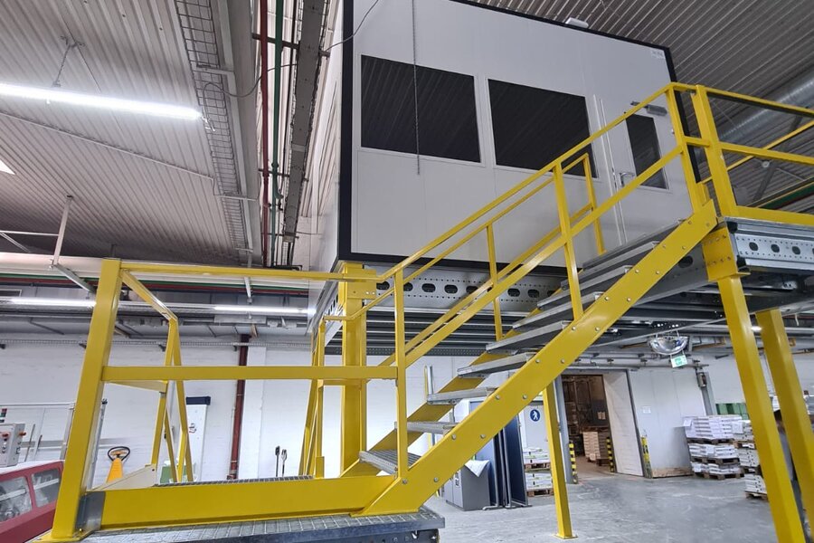Hallenbüro auf gelber Stahlbühne mit Treppe sorgt für erhöhten Stauraum. Verbaut durch Jansen Systembau